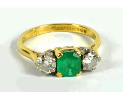 An 18ct yellow gold ring centred with an emerald cut emerald flanked by two round cut diamonds, each approx 0.25cts, in high 