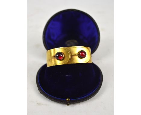 A Victorian yellow metal hinged bangle set with two garnet coloured circular cabochons and housed in a velvet lined gilt tool