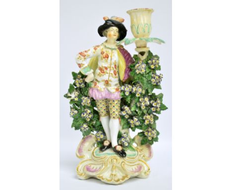 An 18th century Derby figural candlestick modelled as a young man wearing elaborate clothes beside bocage, single candle scon