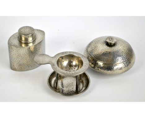 TUDRIC; a pewter hammered powder box, diameter 12cm, a tea caddy, number 0614 and a tea strainer with stand, number 01071 (3)