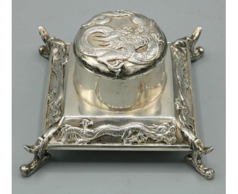 Early C20th Chinese silver square inkwell, hinged cover and tapering base relief decorated with dragons, on four scroll feet,