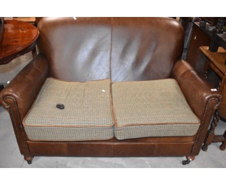 A modern tetrad leather two seater settee, with tweed style loose cushions (damage to castor)