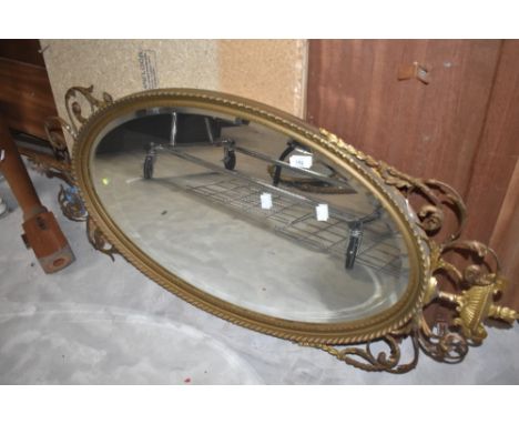 An oval wall mirror having gilt frame with urn and foilate scroll decoration