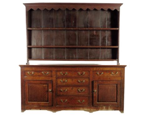 A George III oak dresser, the raised plate rack with a wavy edge frieze and with three shelves, the base fitted with an arran