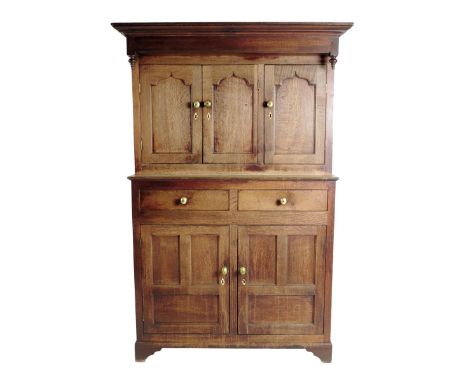 A George III Welsh oak press cupboard, with turn pendant finials above three ogee panelled doors, each enclosing a shelf abov