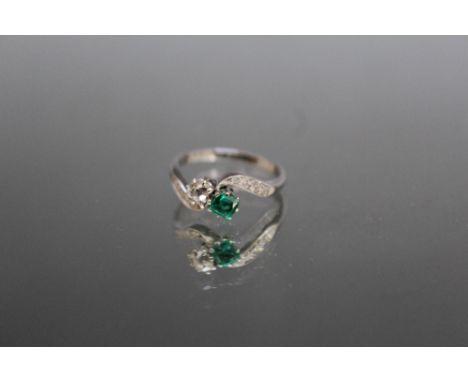 AN EMERALD AND DIAMOND CROSSOVER RING, set with a central old cut diamond of an estimated 0.20 carat and a similar sized emer