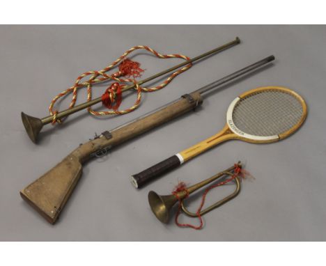 Two brass horns, a vintage tennis racket and a model gun.