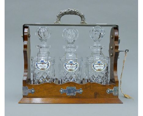 A silver plate mounted mahogany three bottle tantalus with Crown Staffordshire porcelain decanter labels. 33 cm wide.