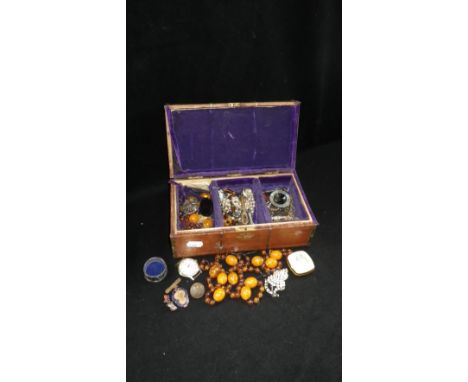 A wooden casket-shaped box containing faux amber bead necklaces and other vintage costume jewellery and badges