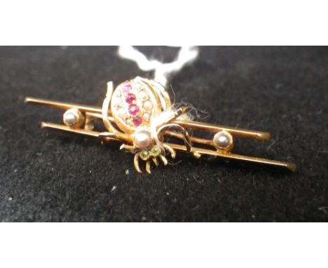 An Edwardian bar brooch, modelled as a spider, with ruby, peridot and seed pearl body in unmarked yellow metal