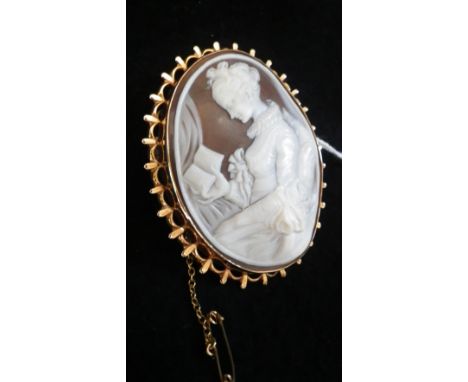 An oval shell cameo depicting a portrait of a woman reading a book, enclosed within a 9ct yellow gold brooch frame with safet