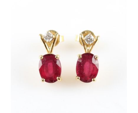 A pair of treated ruby and diamond drop stud earrings, set with an oval cut glass-filled ruby dropper, surmounted with a roun