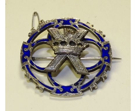 A white metal and blue enamel brooch, in the style of Alexander Ritchie, decorated with crown over cross to centre with folia