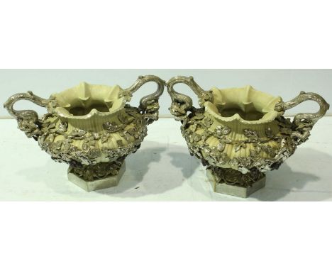 A pair of modern ceramic urns of reeded form, the beige bodies encrusted with silvered fruiting vines, raised on hexagonal pe