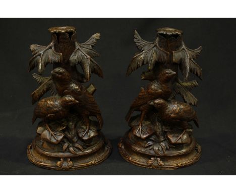 A pair of 19th century German Blackforest carved candlesticks, each formed as s pair of partridges stood before a tree trunk 
