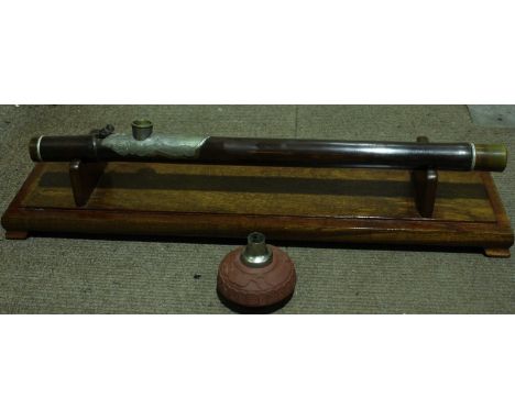 An early 20th century Oriental metal mounted opium pipe, with terracotta reservoir, in a hardwood and glass display case.