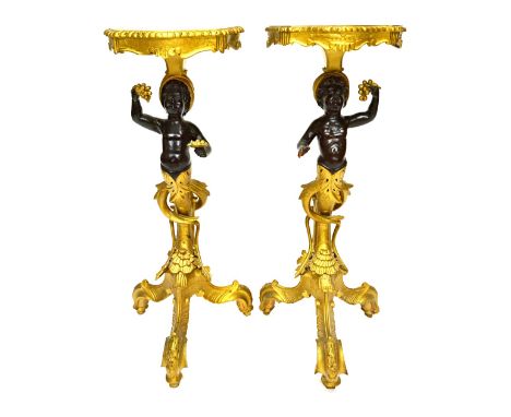 A pair of 19th century ebonised and gilded stands, with shaped tops and blackamoor figural supports, on scrolling tripod base