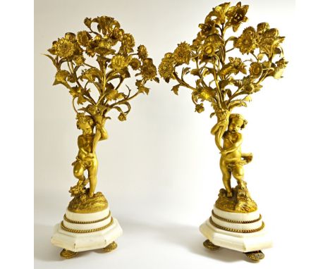 A pair of French ormolu six branch figural candelabra, late 19th century, each cupid figure modelled and cast holding a cornu