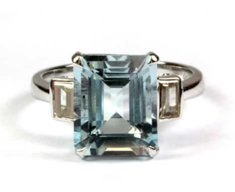 An 18ct white gold (stamped 750) ring set with an emerald cut aquamarine flanked by baguette cut fancy light brown diamonds, 