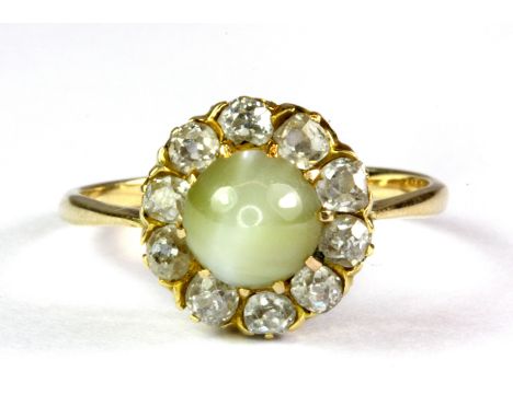 A yellow metal (tested high carat gold) cluster ring set with a cabochon cut chrysoberyl cat's eye surrounded by old cut diam