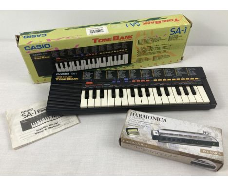 A boxed vintage 1980's Casio SA-1 Tone Bank battery operated keyboard. Together with a boxed stainless steel harmonica. Casio