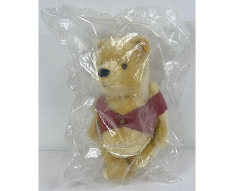 A 10.5" Steiff blond mohair, fully jointed Winnie-the-Pooh teddy bear. With red jacket. In sealed and unopened plastic packag