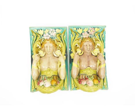 A pair of large architectural tiles probably Maw & Co, each modelled as bare breasted classical maiden with swag of fruit bef