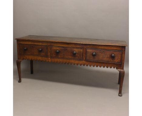 AN OAK DRESSER BASE. 19th century, with three drawers and turned handles above a carved apron on cabriole front legs, height 