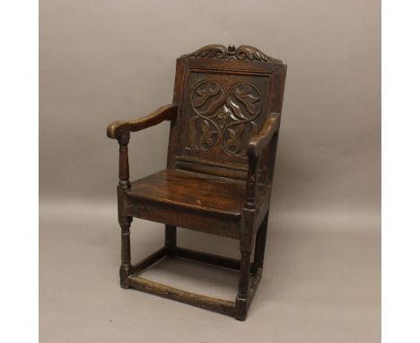 AN OAK WAINSCOT CHAIR. late 17th or early 18th century, the floral carved top rail above a panelled back and solid seat on tu