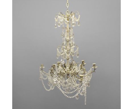 A TWELVE LIGHT CRYSTAL CHANDELIER. early 20th century, with four tiers of glass drops and swags above scrolling brass branche