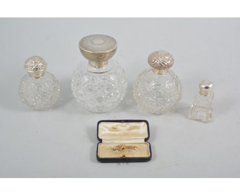 Four vintage silver topped glass perfume bottles, engine turned and repousse chased covers, star cut bases to three larger bo