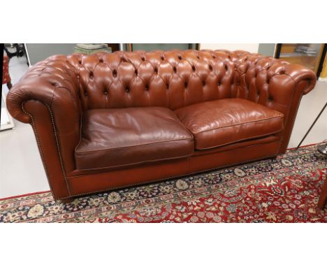 A two-seater Chesterfield sofa and armchair with ottoman, 20th century. Brown leather padded upholstery, raised backrest, up 