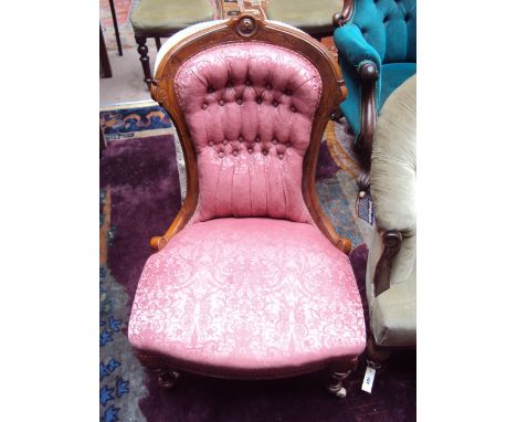 A Victorian walnut nursing chair with carved frame and waisted button back upholstered back, on turned forelegs and ceramic c