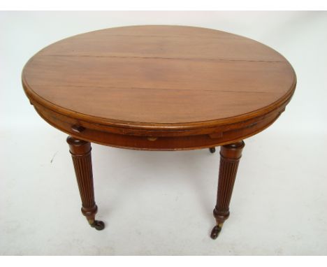 A late Victorian extending circular dining table, on tapering reeded legs, on ceramic casters, with extra single leaf and win