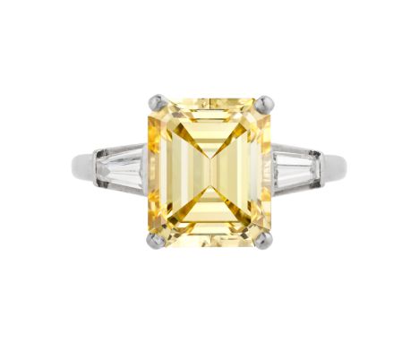 A 5.46 CARAT FANCY INTENSE YELLOW DIAMOND RING in platinum, set with an emerald cut yellow diamond of 5.46 carats, accented o