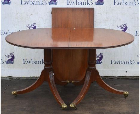 A Regency style mahogany twin pillar dining table, with one leaf insertion, the supports with reeded sabre legs ending in bra