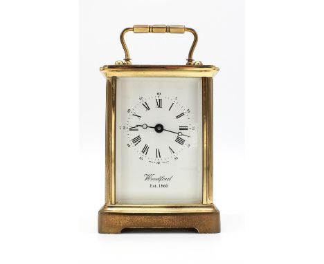 A modern brass cased carriage clock, the white enamel dial detailed 'Woodford Est 1860', with visible escapement and a brass 