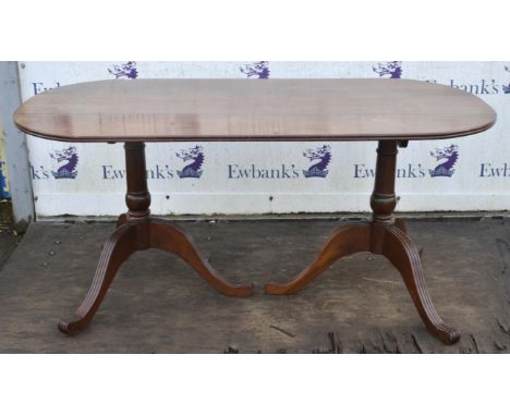 A Regency style mahogany dining table, the triple plank top with a moulded edge and rounded ends, on twin pillar bases with s