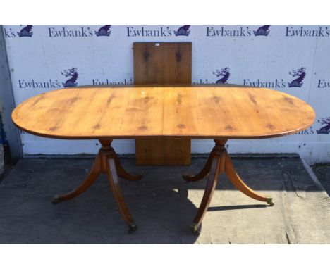 A Regency style yew wood and mahogany twin pillar dining table, with one leaf insertion, the top crossbanded, the legs ending