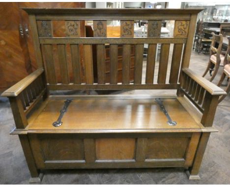 An Arts &amp; Crafts golden oak monks hall seat bench with carved floral panels to the back and a three panel style coffer fr