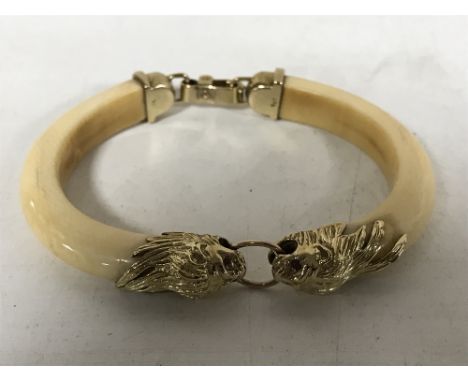 A 1920's two-piece ivory bangle, with 9ct gold mounts formed as lions with ruby set eyes