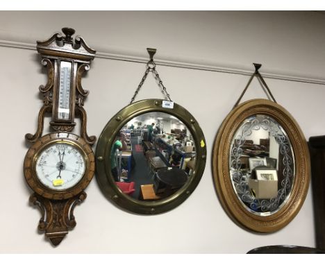 An oval gilt framed etched mirror, brass port hole mirror and a carved oak barometer 