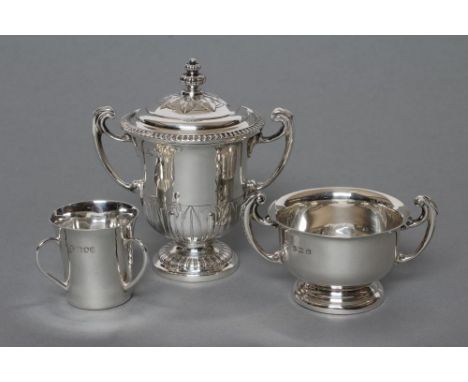 A SMALL TWO HANDLED SILVER TROPHY AND COVER, maker's mark GH, Sheffield 1937, the "U" shaped bowl with stiff leaf chased base