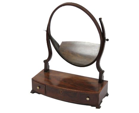 An early 19thC mahogany table mirror, the oval glass flanked by S scroll styles, on a bow front base, with a wide cross bandi