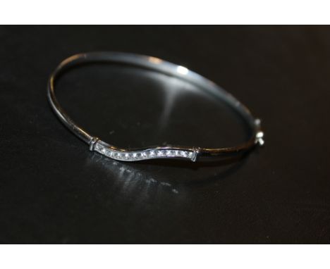 A 9KT WHITE GOLD WAVY BAND BANGLE WITH TWELVE CHANNEL SET BRILLIANT CUT DIAMONDS