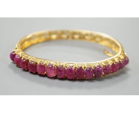 A modern Thai yellow metal and graduated fifteen stone cabochon ruby set hinged bangle, interior diameter 54mm, gross weight 