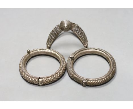 Two 20th century Indian white metal hinged bracelets and a similar shaped bangle.