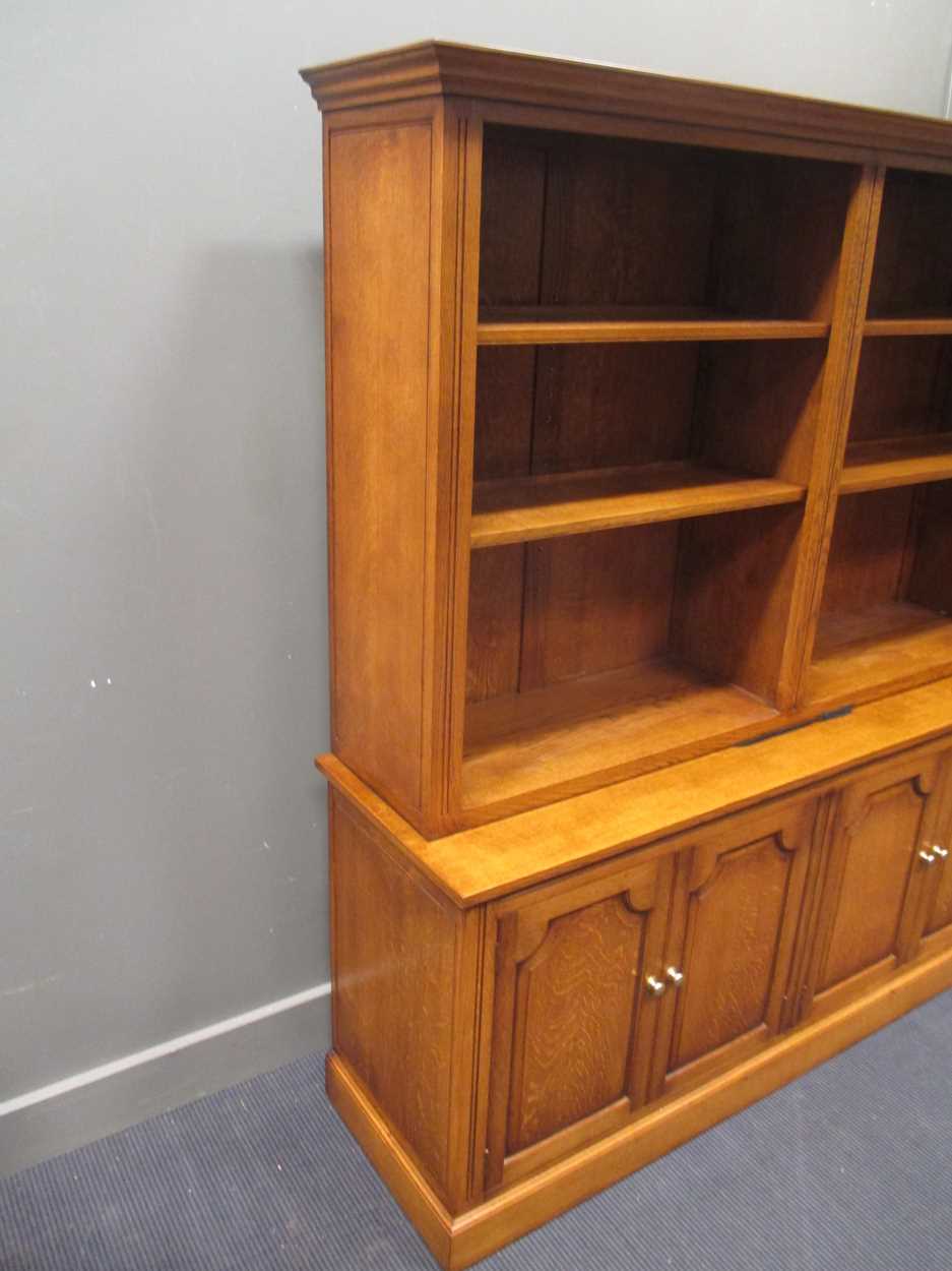 A modern oak bookcase with open shelves above cupboards, enclosed by