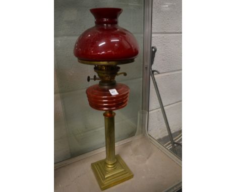A brass and cranberry coloured glass oil lamp with a shade.