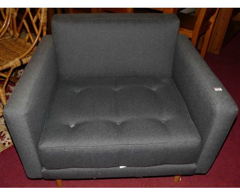 A contemporary grey upholstered single armchair, having reverse buttoned cushion seat raised on turned light oak supports, wi